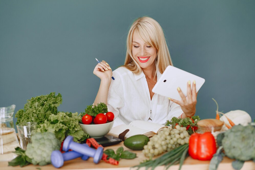 A woman at a table with vegetables and a tablet, brainstorming restaurant slogan ideas