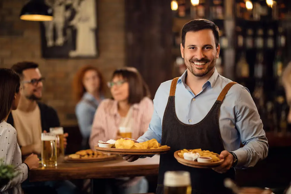 Smiling waiter serves food in busy restaurant, demonstrating excellent restaurant reputation management practices